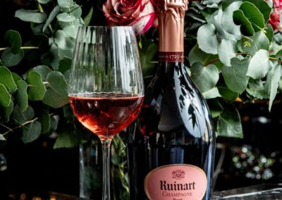 Champagne ruinart rosé dans un verre avec la bouteille sur fond fleuri